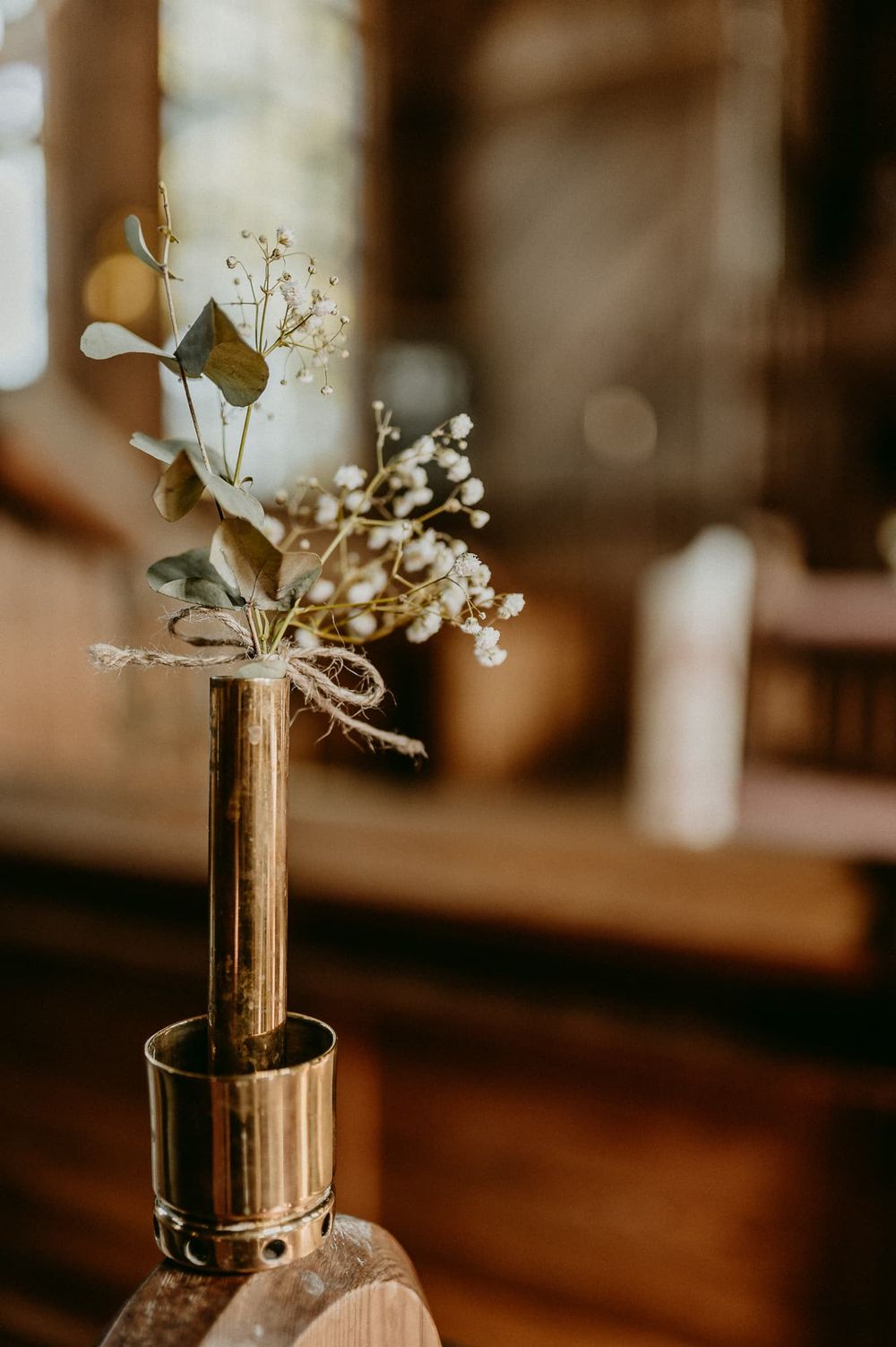 Vit blomma i guldfärgad vas som sitter på en bänkrad i Bjurbäcks kyrka.
