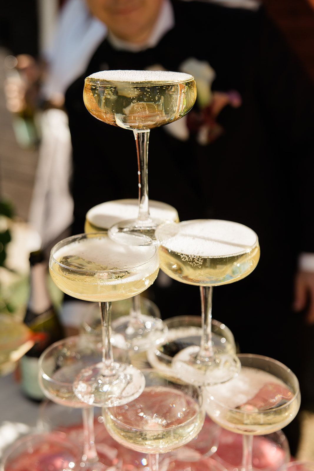 Elegant champagne coupe glasses stacked in a tower formation with golden bubbly cocktails at a formal event.
