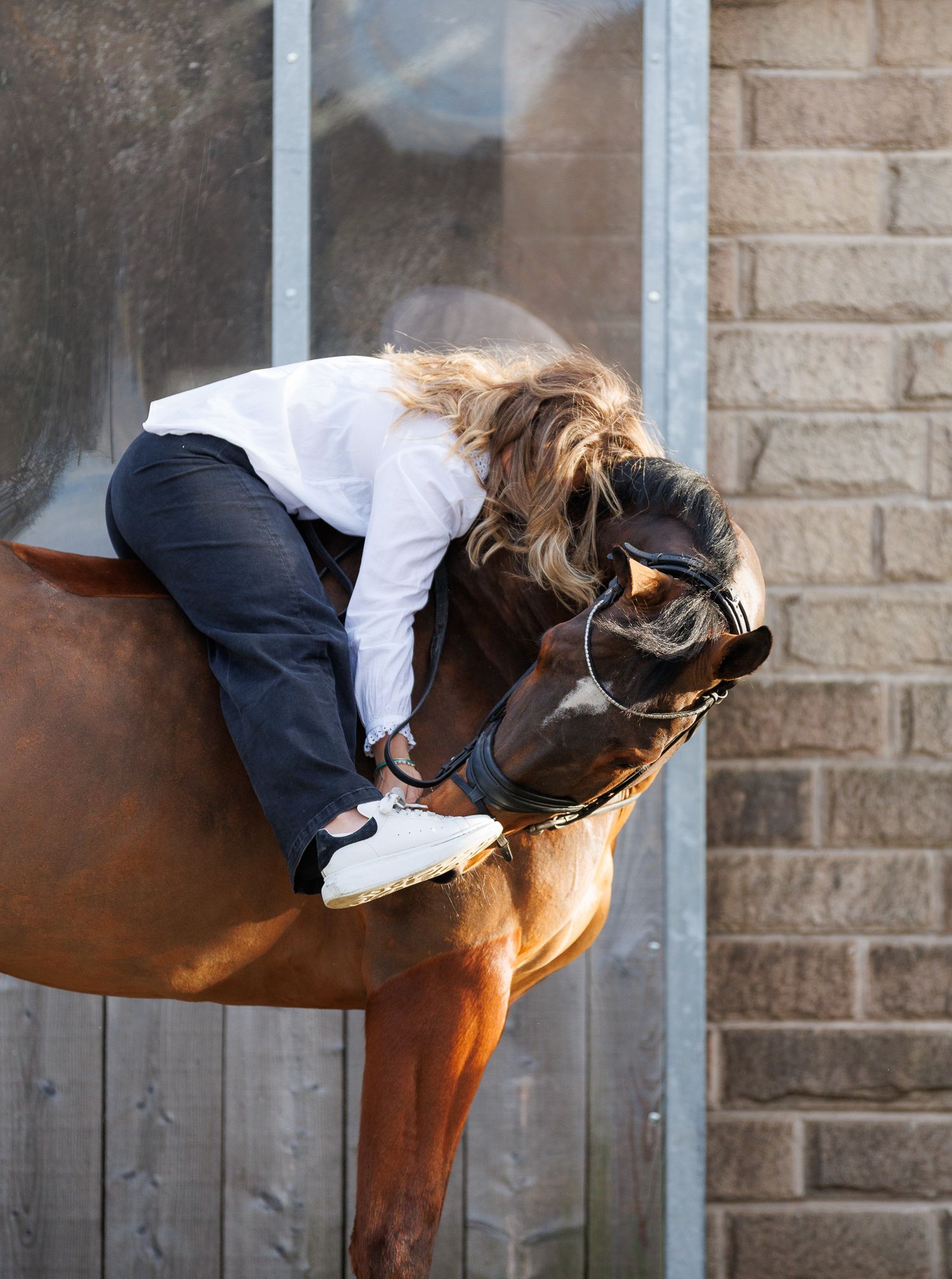 A brown horse and rider in a white sweater pose together against autumn foliage in soft natural lighting.