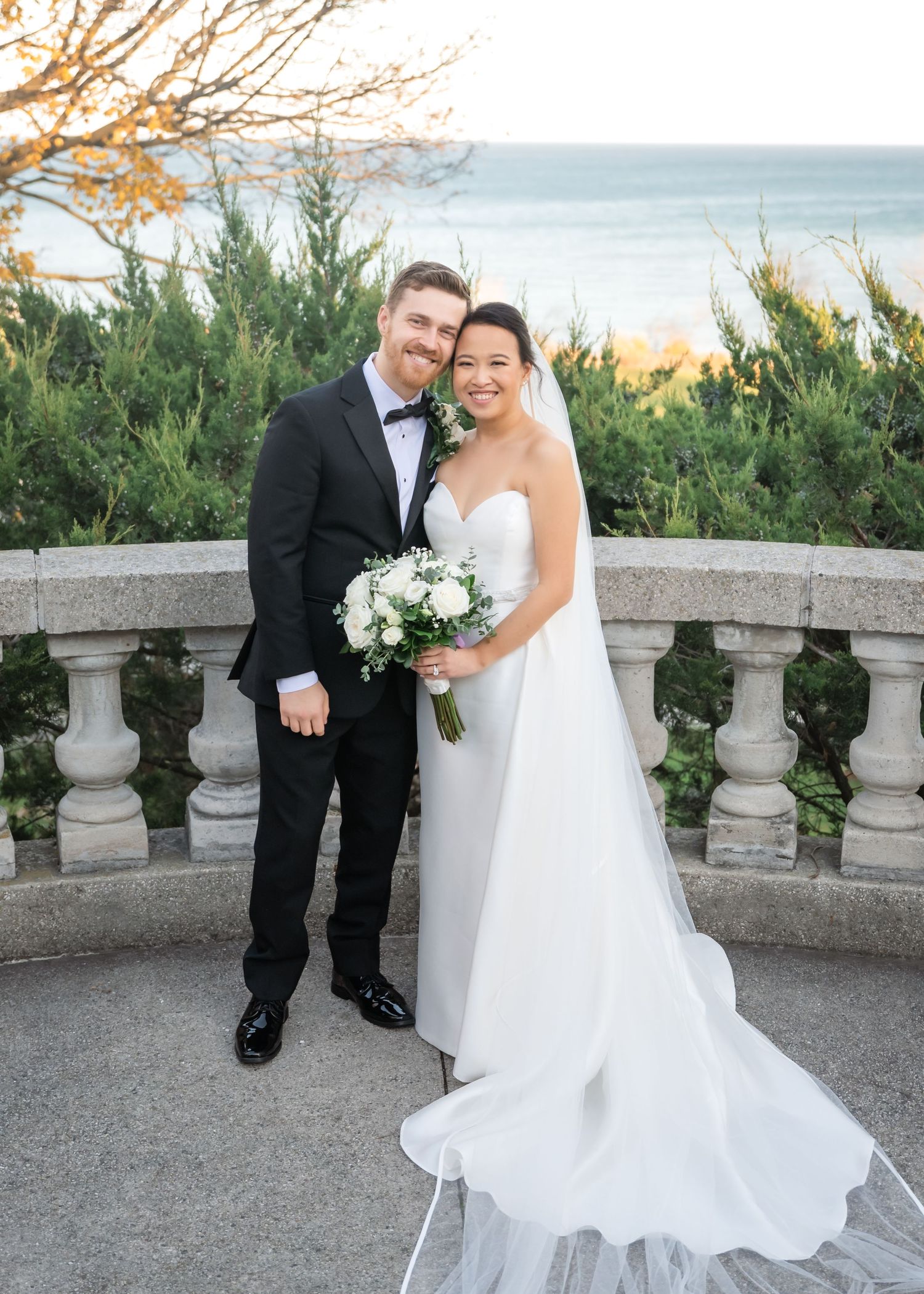 A romantic autumn wedding photo near a stone lion statue with a flowing cathedral veil and vintage lamp post at sunset.