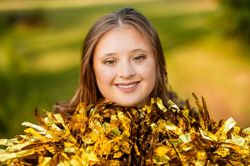 Gold pom poms create festive border around cheerleader portrait in natural lighting.