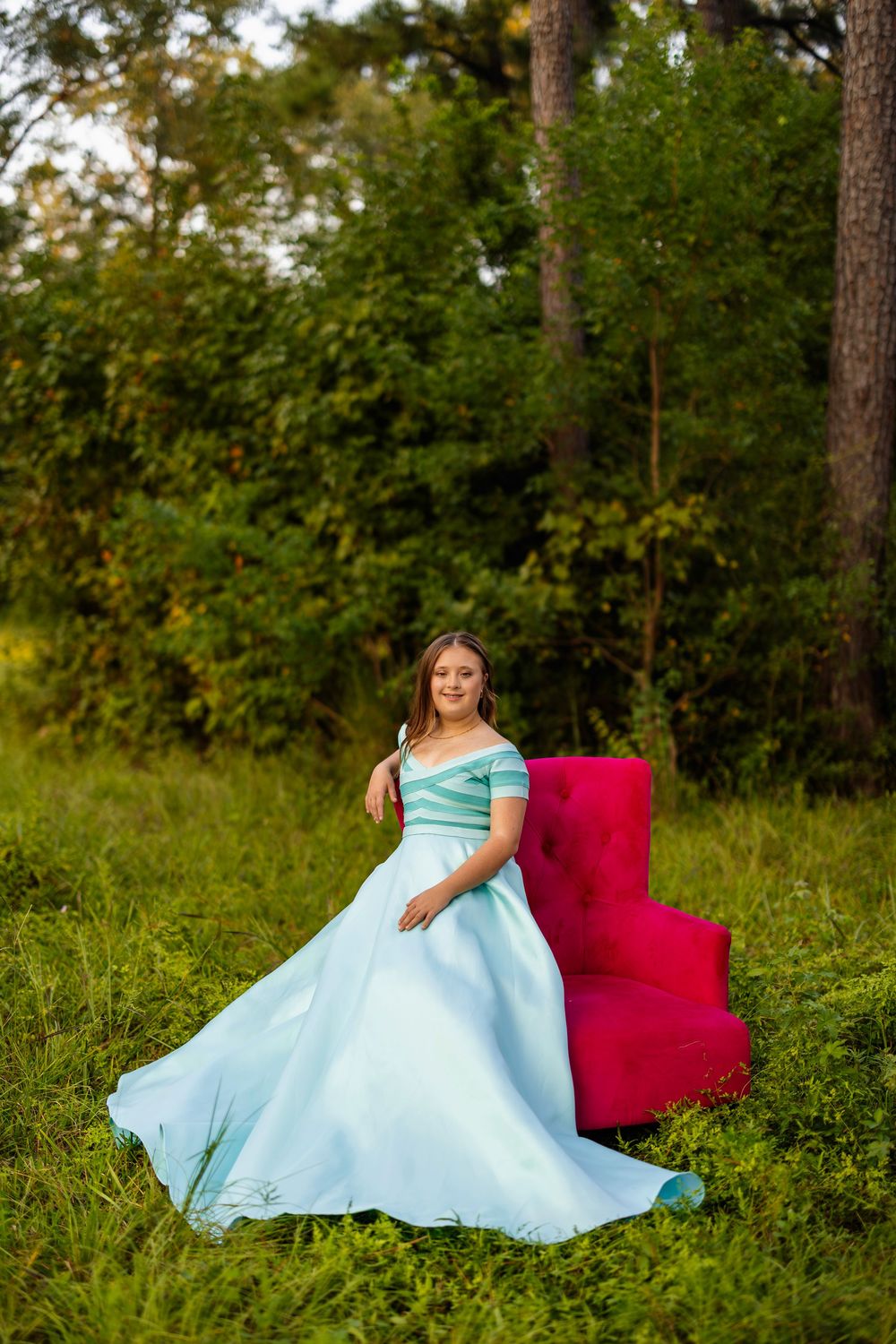 Elegant mint dress photoshoot with red chair accent in natural outdoor setting.