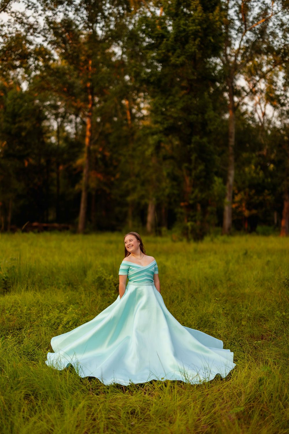 Flowing mint green formal dress twirls in outdoor garden setting at sunset.