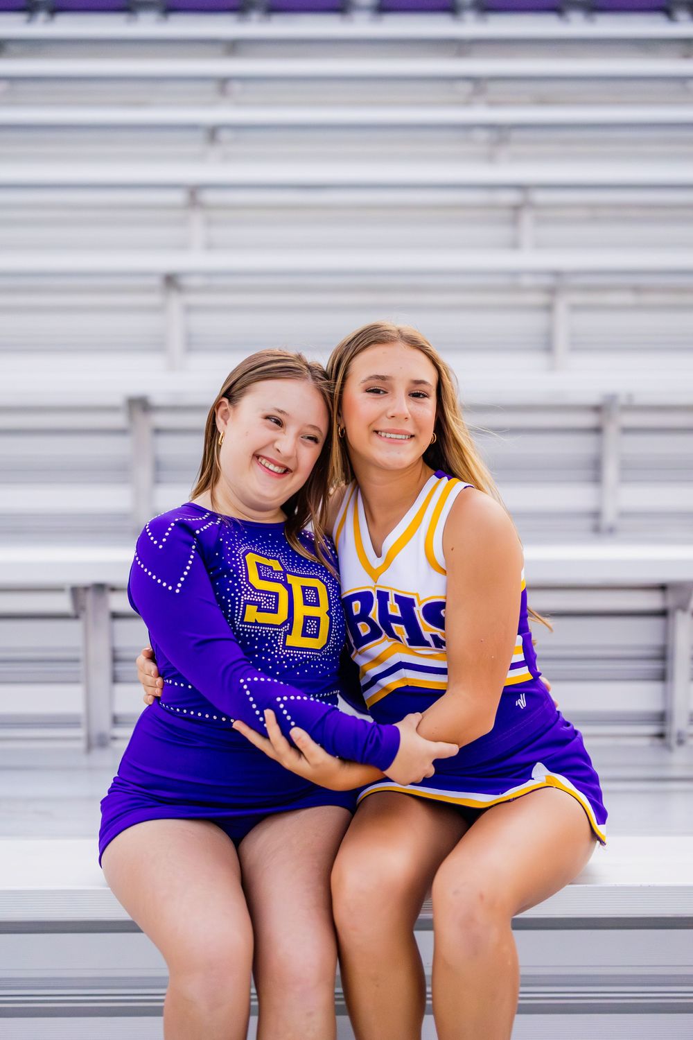 Cheerleaders in purple uniforms pose together on stadium bleachers.