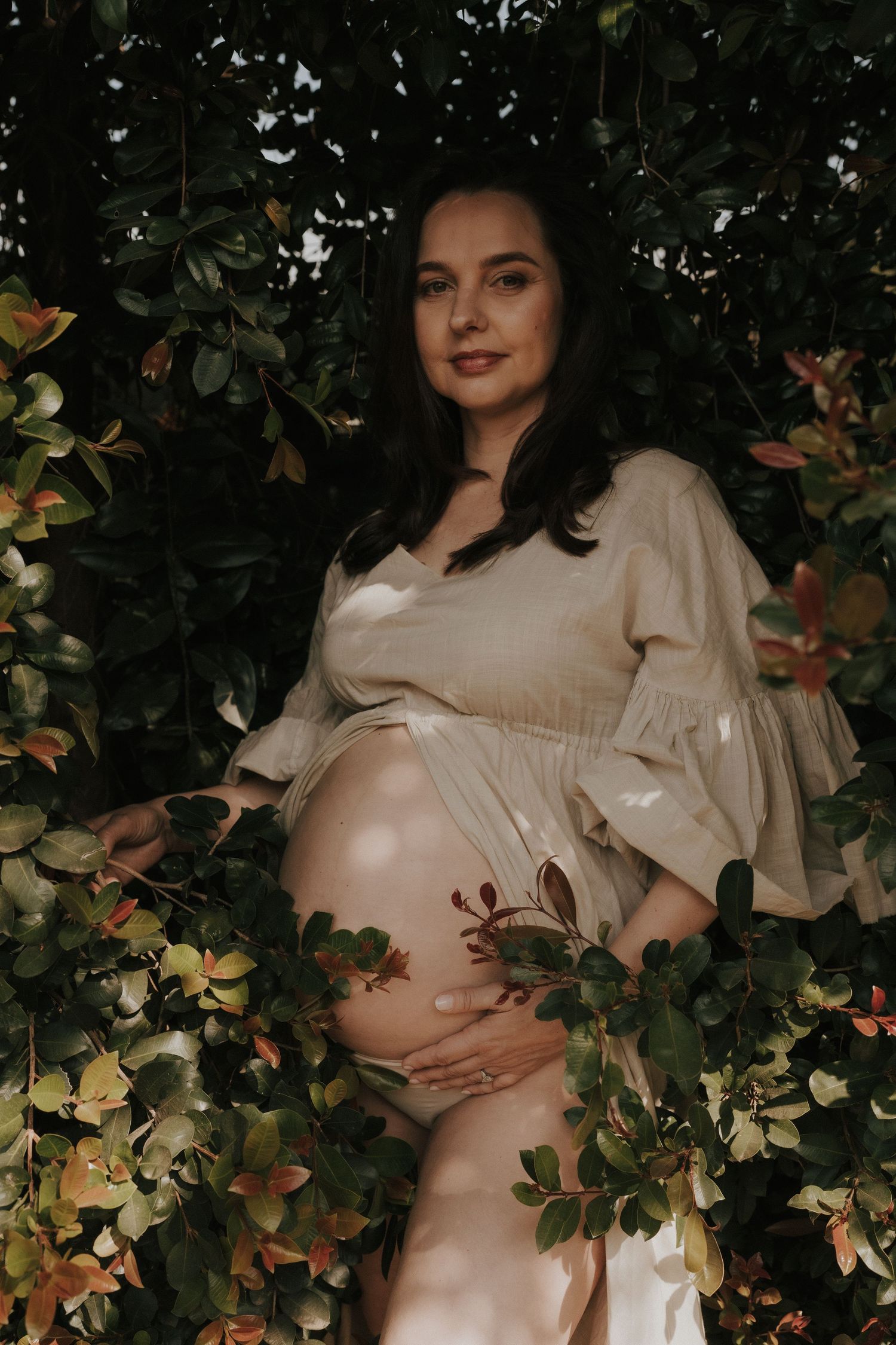Artistic maternity photo with pregnant belly surrounded by green foliage and flowers.