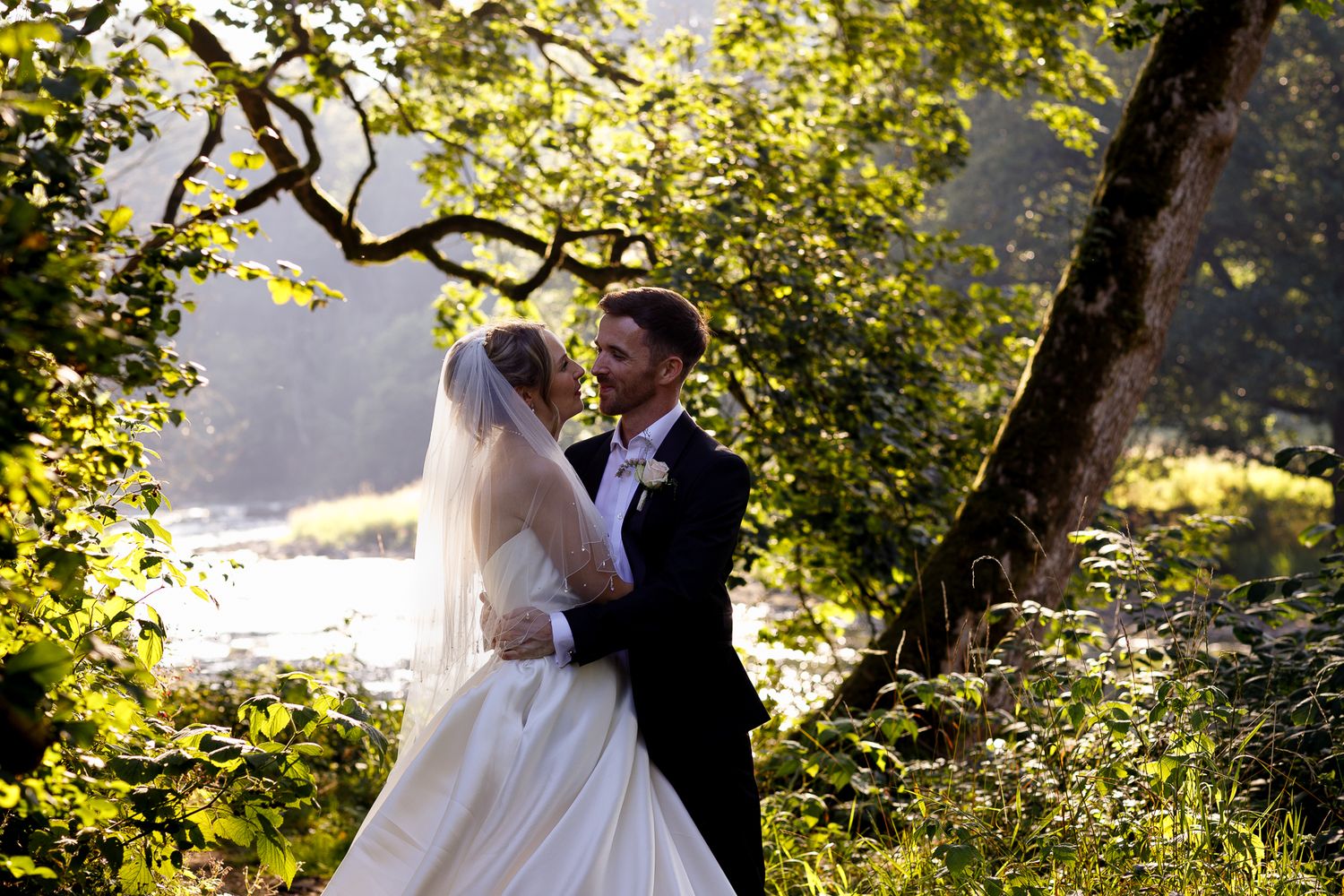 A couple shares a romantic moment in a sunlit garden setting during their wedding celebration.