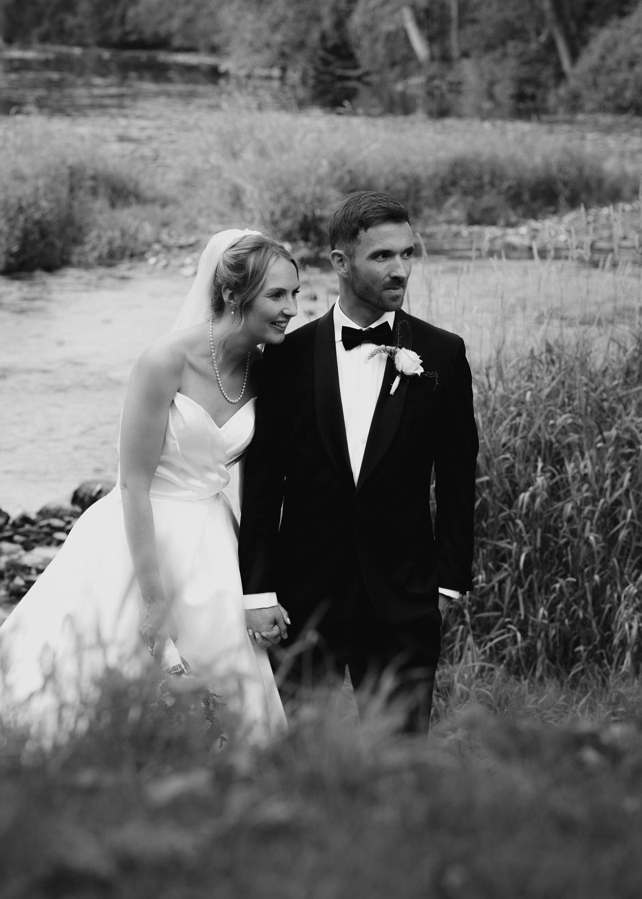 A romantic black and white wedding photo series showing a couple in formal attire sitting together in a meadow.