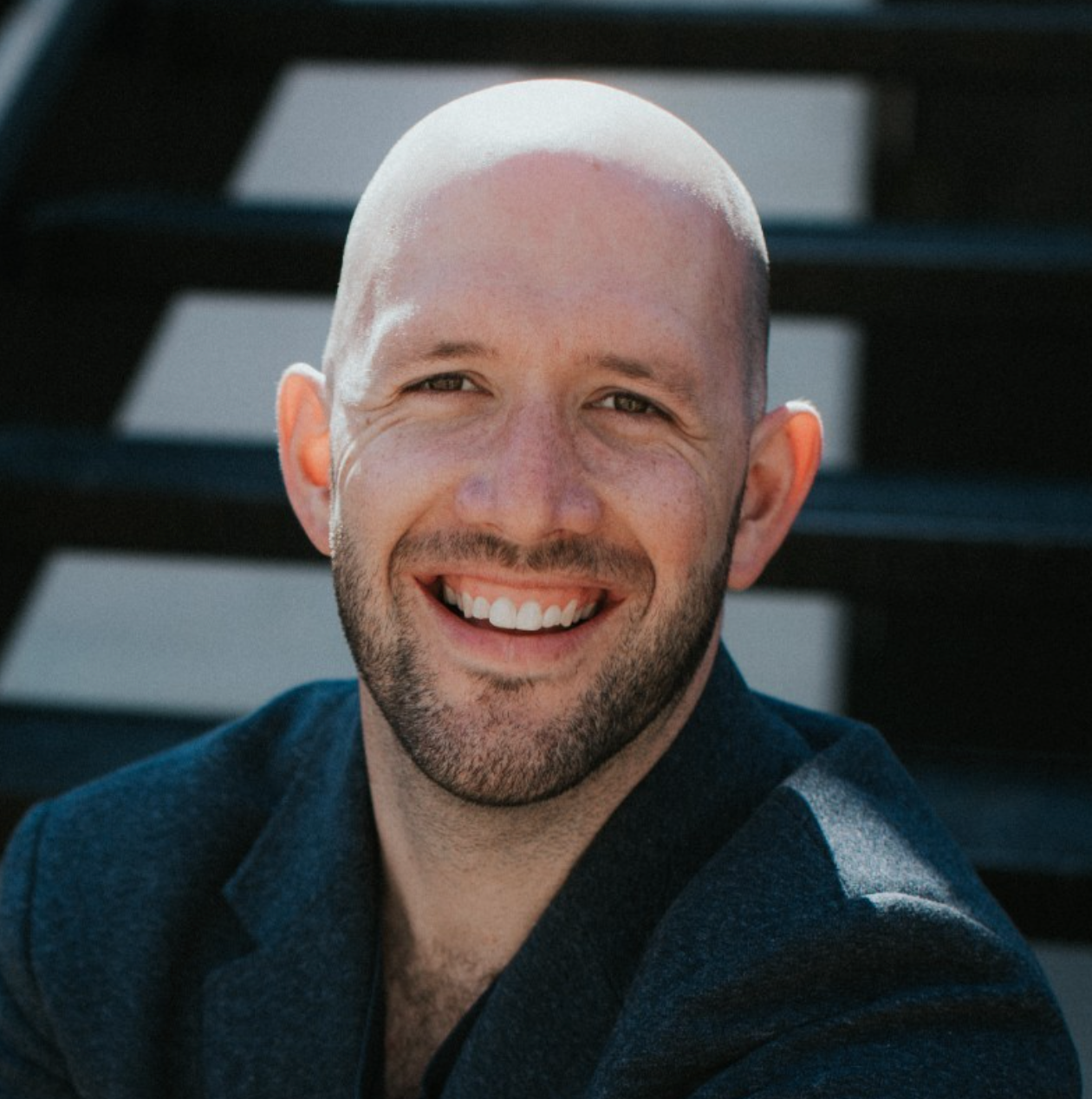 Professional headshot of a smiling person against dark architectural background.