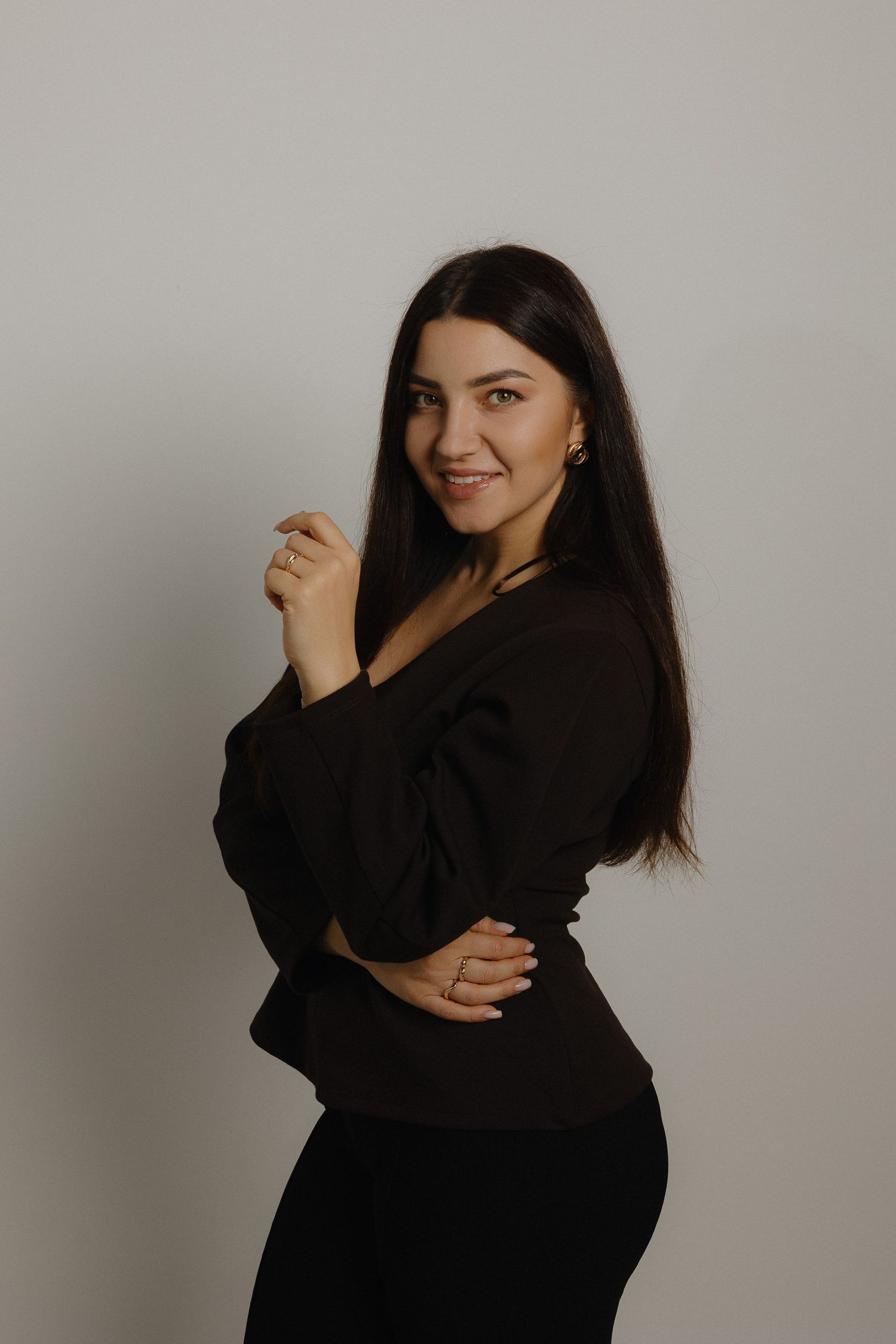 A woman in a black outfit poses against a neutral background in a professional studio portrait.