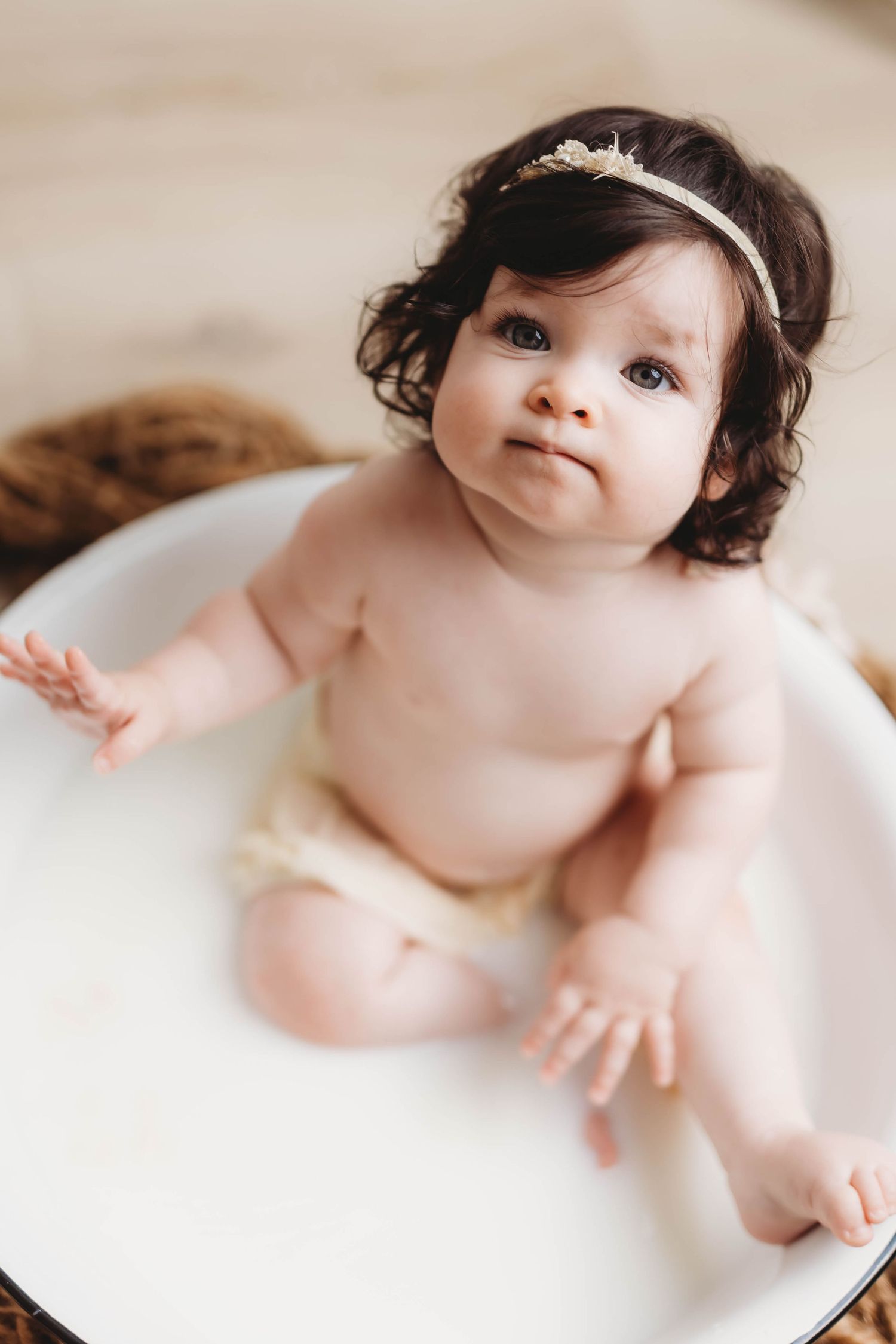 Artistic milk bath photography featuring baby in white enamel basin.