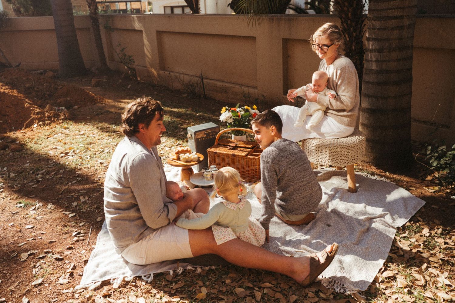 A family enjoys a picnic together on a blanket in dappled sunlight.