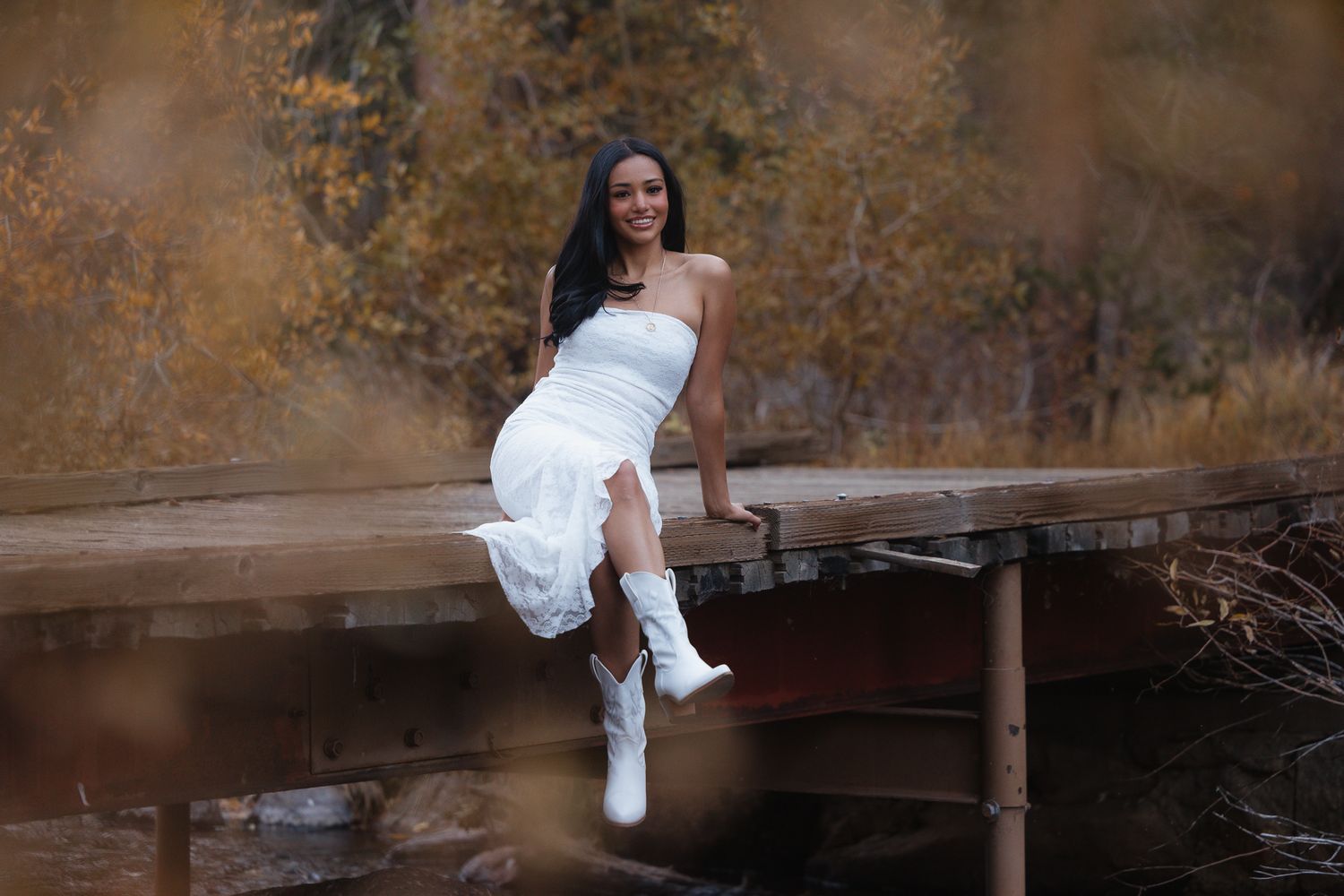 Portrait session in a rustic field with autumn trees and mountain cabin in background.