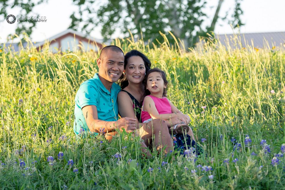 Family of three in a field of bluebonnets, candid moment in natural light.