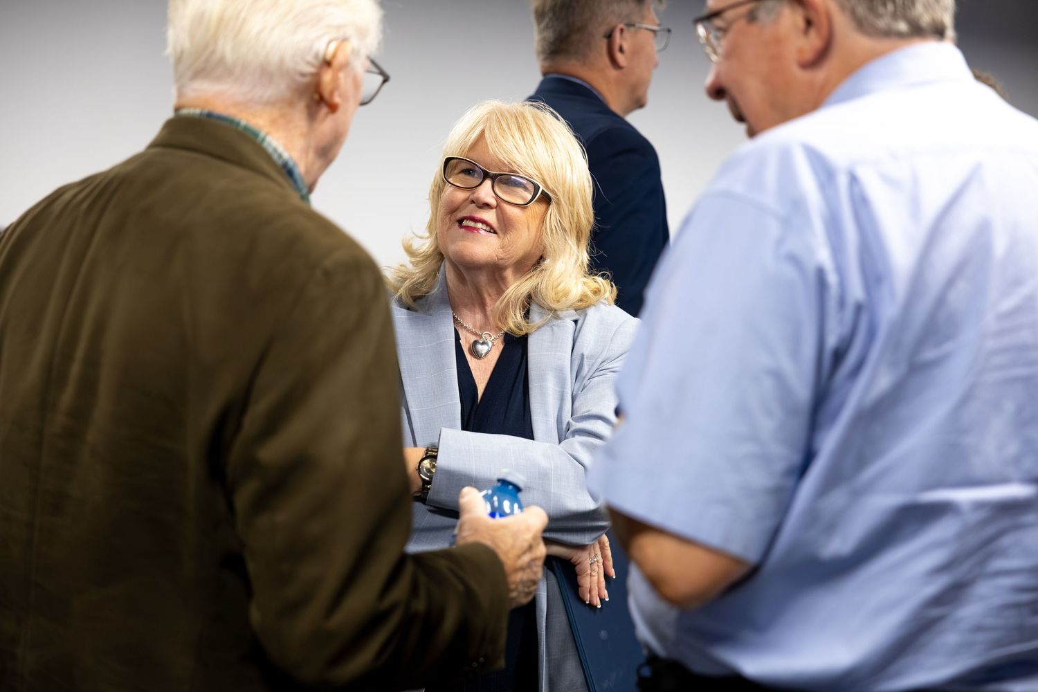 A smiling blonde woman in a blazer engages in conversation with two men at a professional networking event.