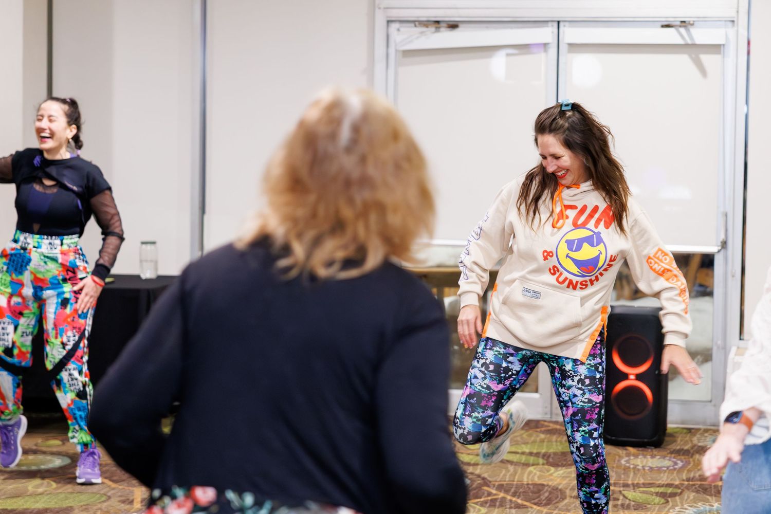 People in colorful patterned leggings participate in a group fitness class in a bright studio space.