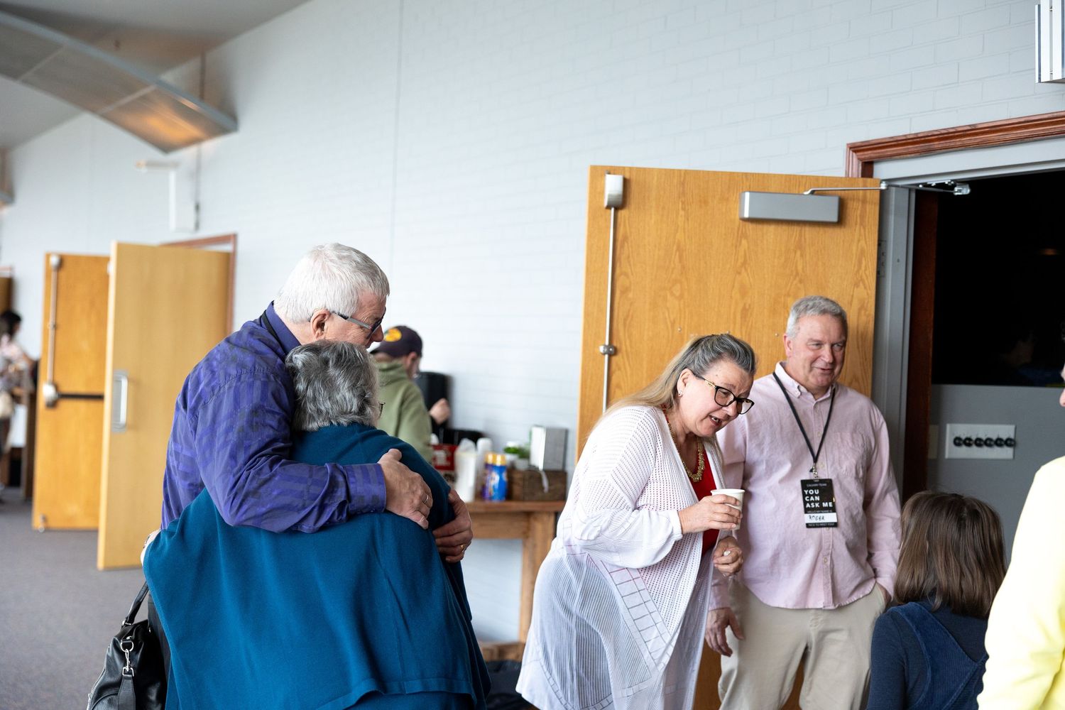 People standing in a line against a white wall with wooden cabinets in what appears to be an office or institutional setting.