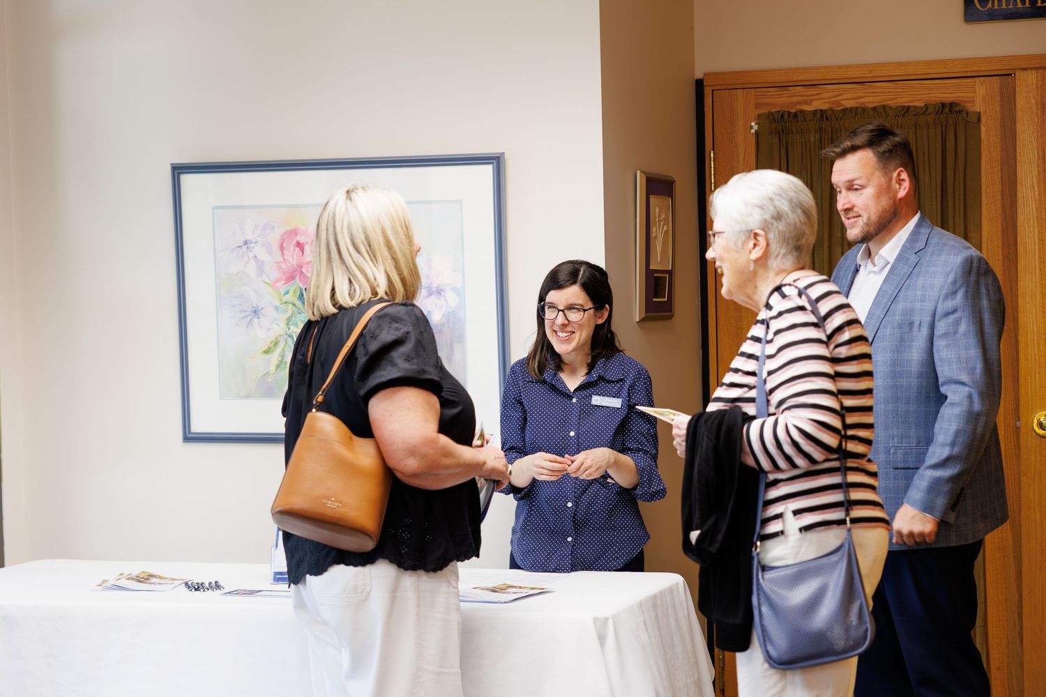 A small group of people gather around a registration table at an event with framed artwork on the wall.