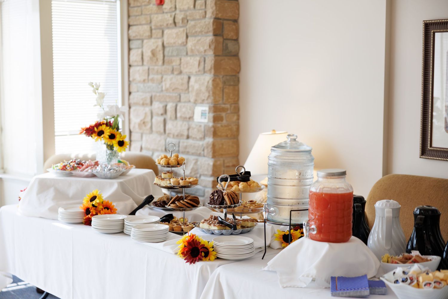 A long banquet table with white linens and stone wall backdrop displays an elegant buffet spread for a catering event.
