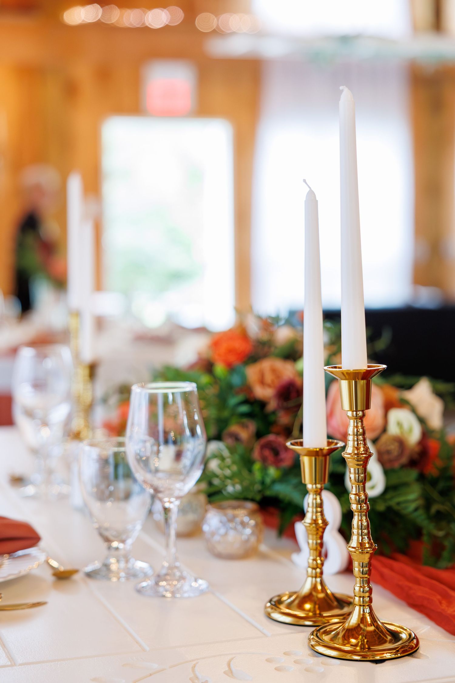 Elegant table setting with white candles in gold candlesticks and evergreen garland decorations for a holiday celebration.