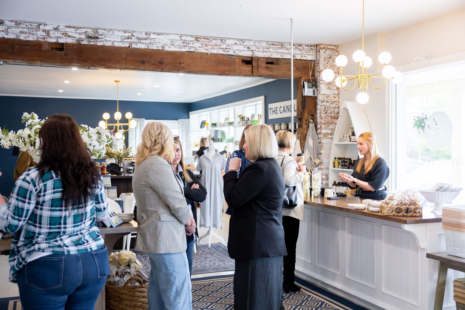 Women socializing at an elegant boutique event with navy walls, exposed brick, and a white bar counter displaying desserts.
