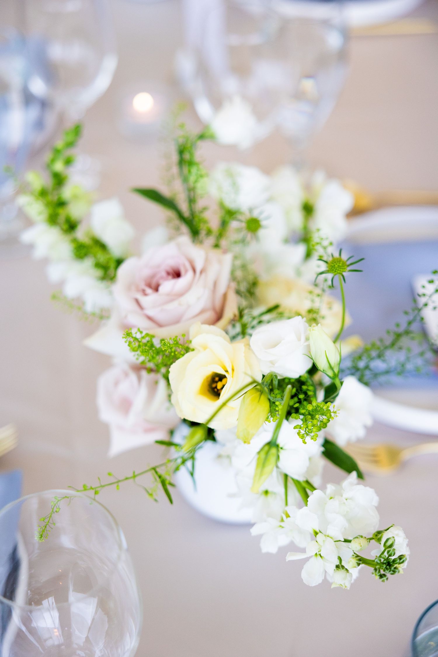 Delicate floral centerpieces with pale pink roses, white flowers and green accents arranged in glass vases on an elegant table.