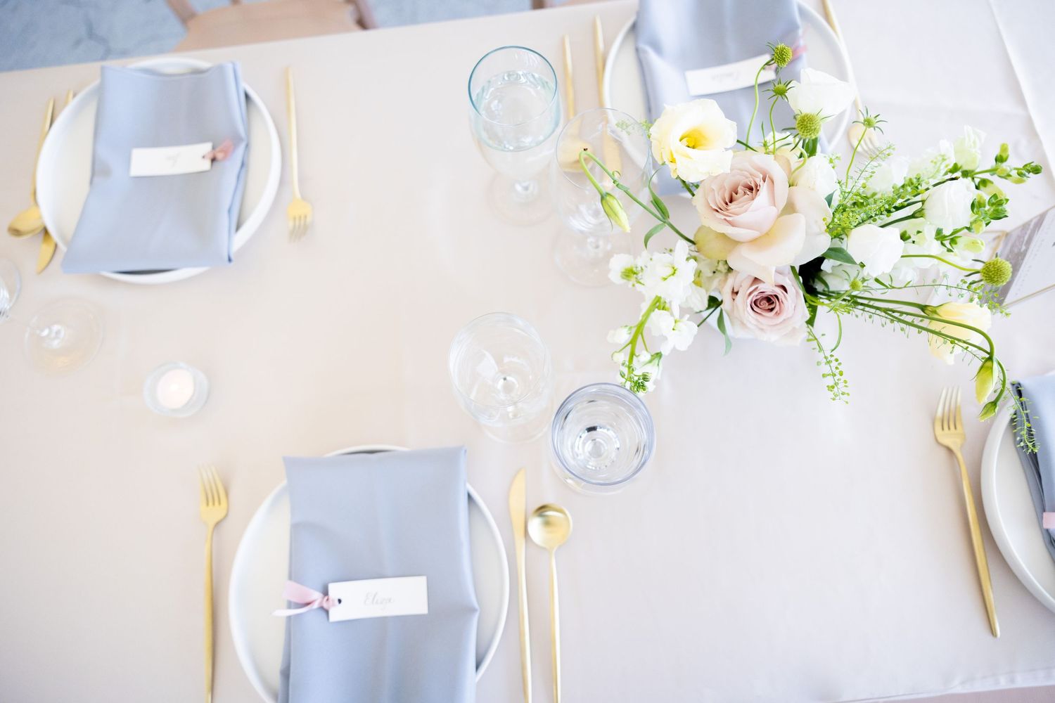Wedding reception table settings with delicate floral centerpieces and soft pink accents in natural light.