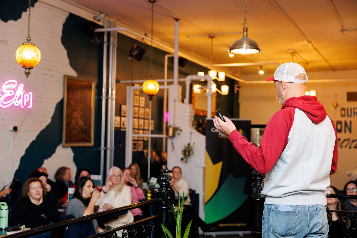 People dancing and socializing in a dimly lit venue with hanging pendant lights and neon signs on the wall.