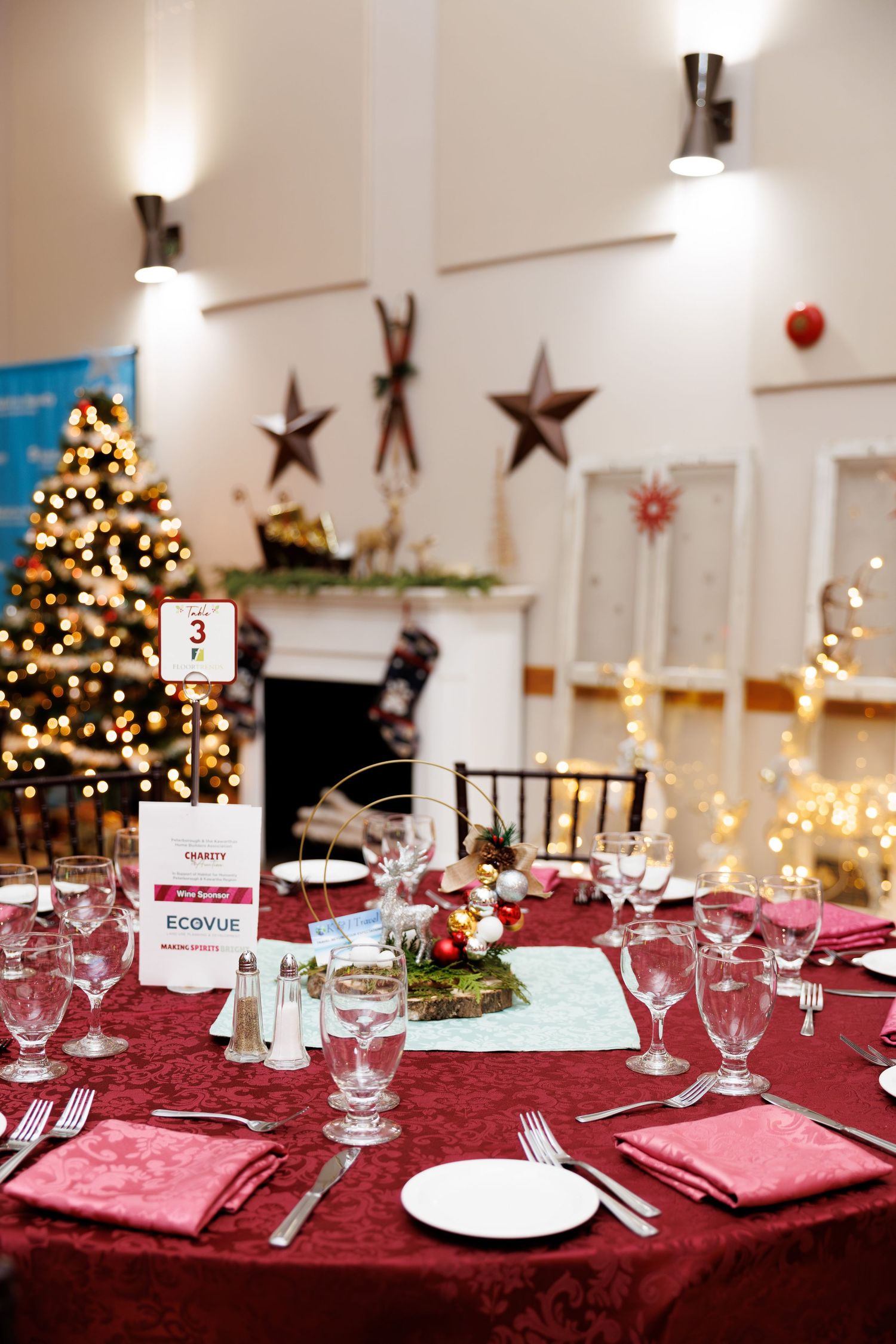 Elegant holiday table settings with red tablecloths, white plates, and Christmas tree decorations in the background.