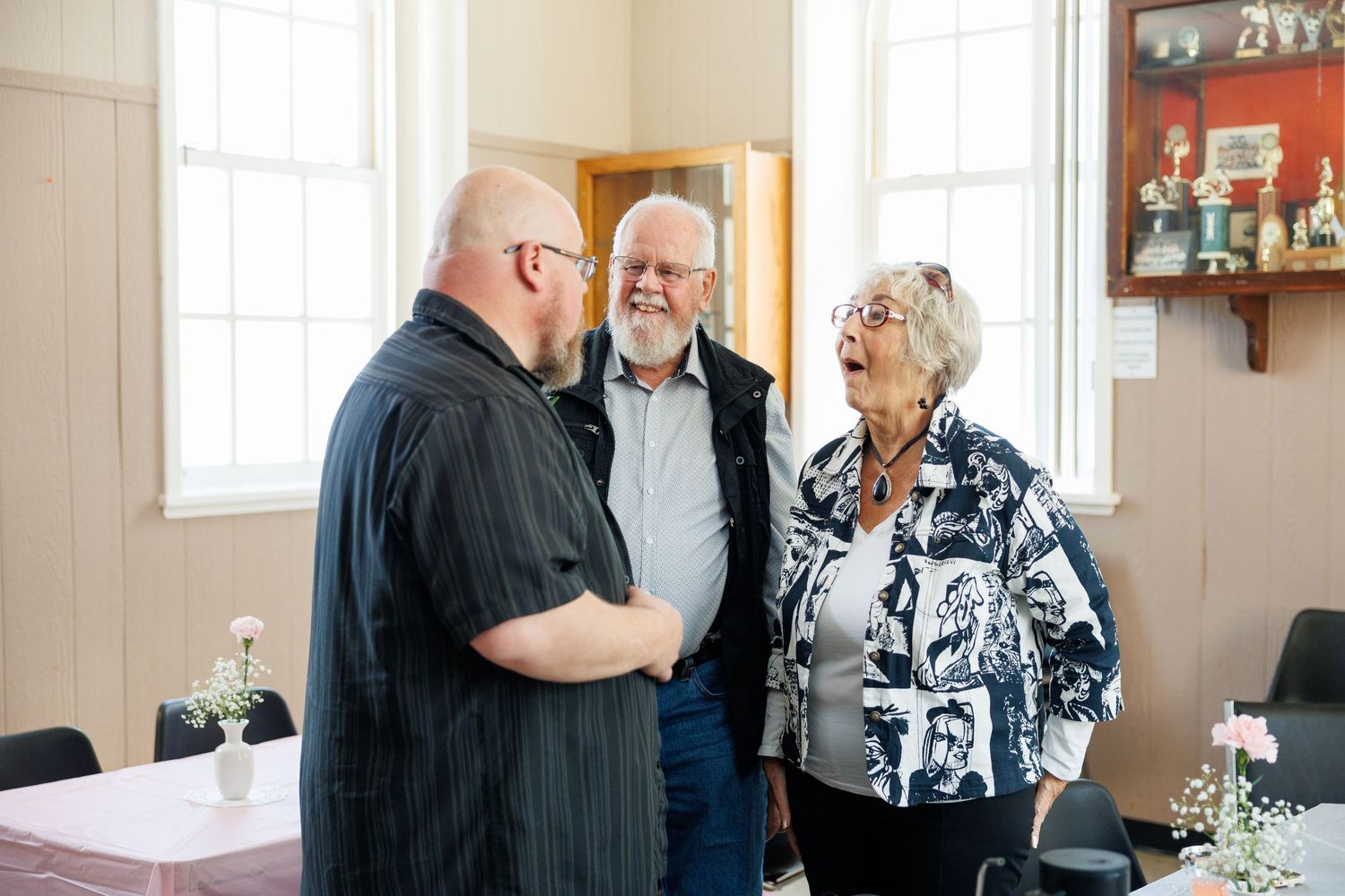 Three seniors sharing a lighthearted conversation in a bright room with display shelves in the background.