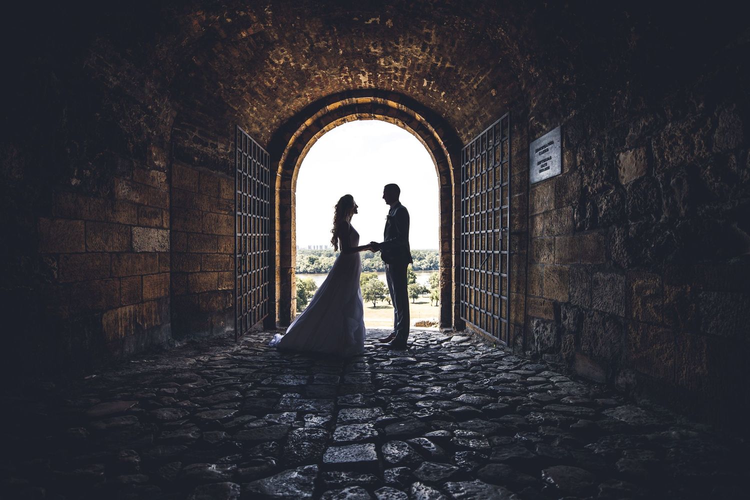 Silhouettes of people walking through dark stone archways and tunnels in an ancient European city.