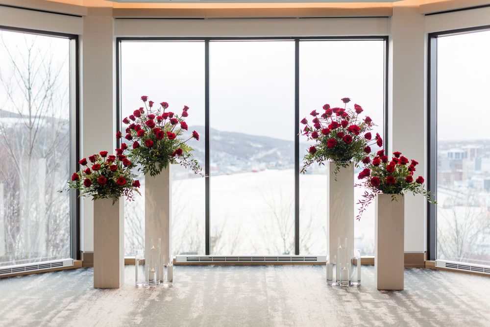 Elegant wedding ceremony setup with red floral arrangements on white pedestals in front of panoramic winter mountain views.