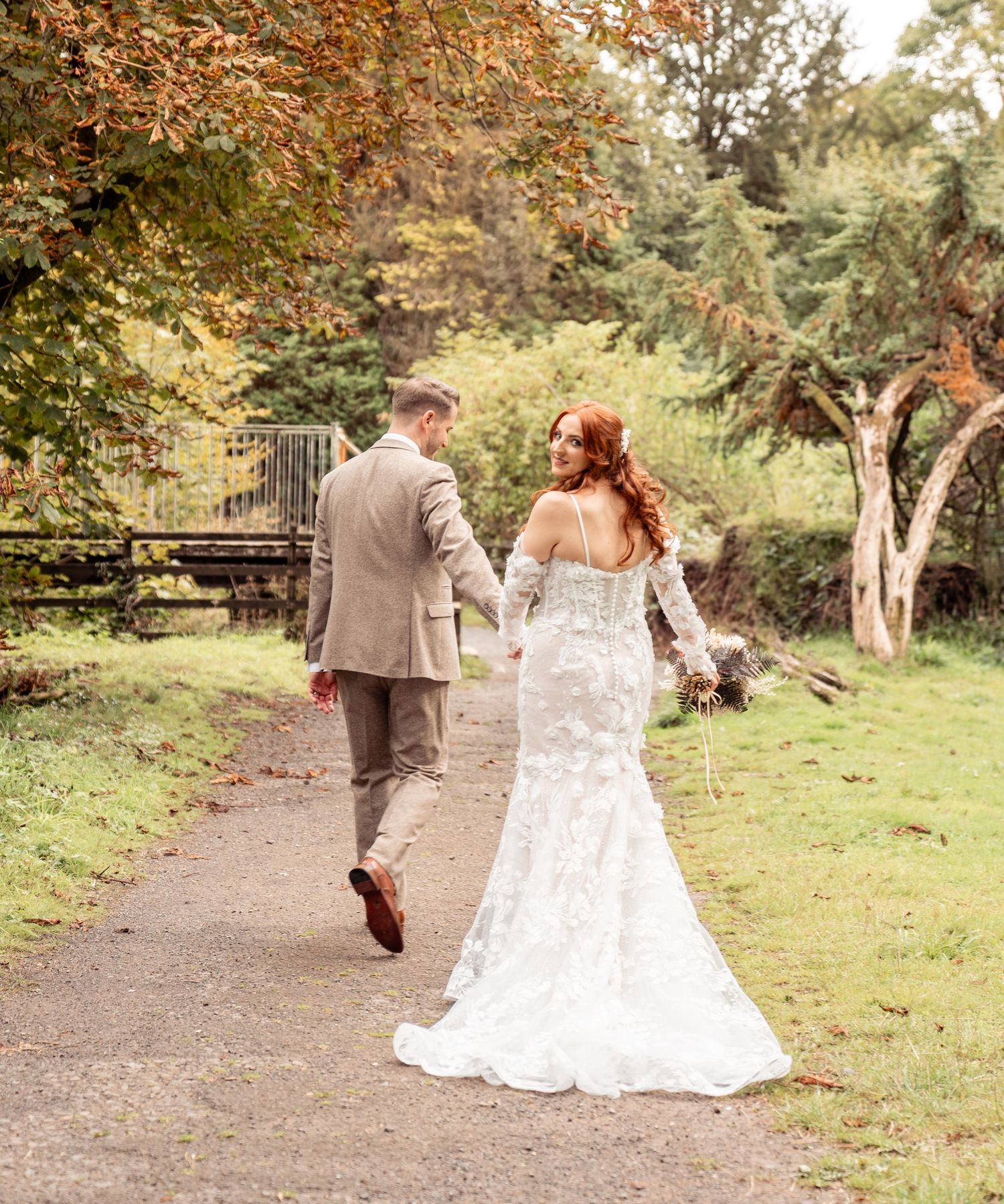A couple walks together on a rustic wooden bridge surrounded by lush greenery on their wedding day.