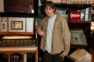 A person browses through vinyl records at a record store while wearing a tan jacket.