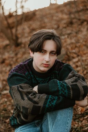 A person in a dark knit sweater sits among autumn leaves in a moody outdoor portrait series.