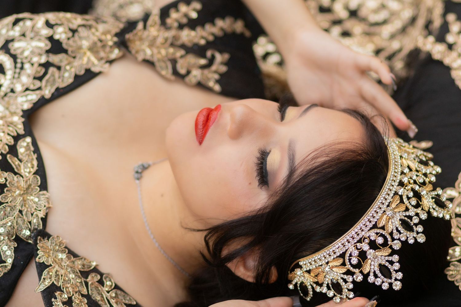 A woman with dark hair lies gracefully among scattered gold decorative elements in an artistic portrait series.