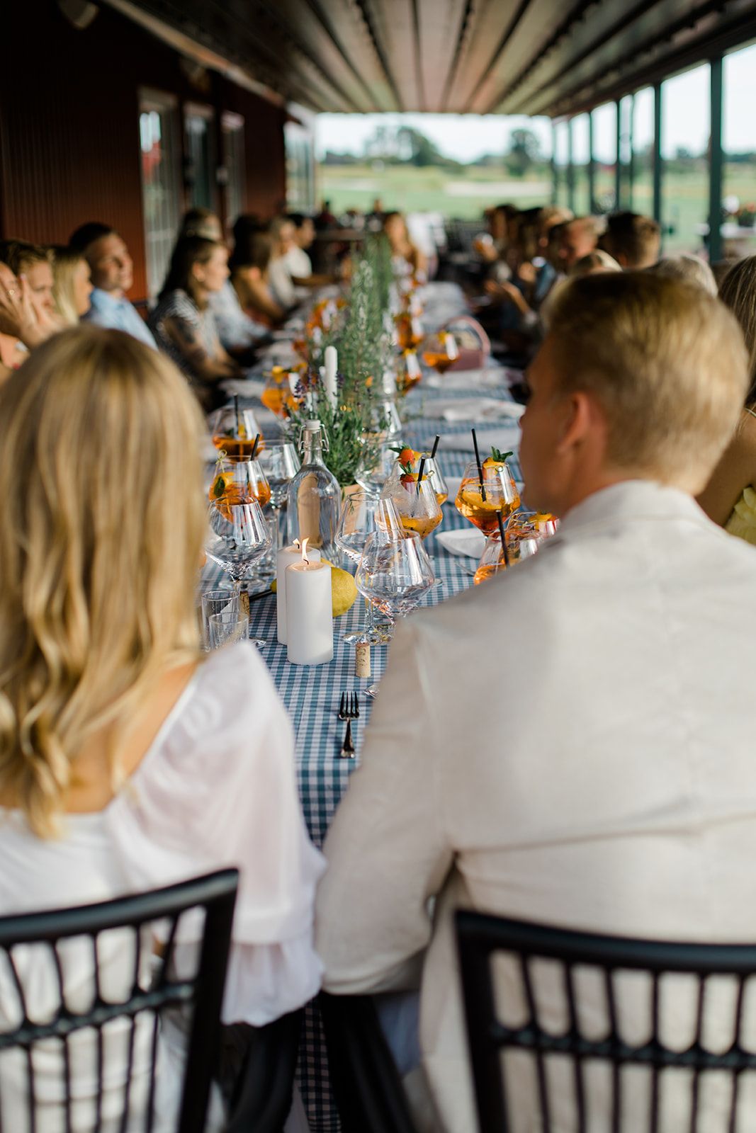Wedding reception table settings with blue gingham napkins and orange floral centerpieces at an outdoor venue.