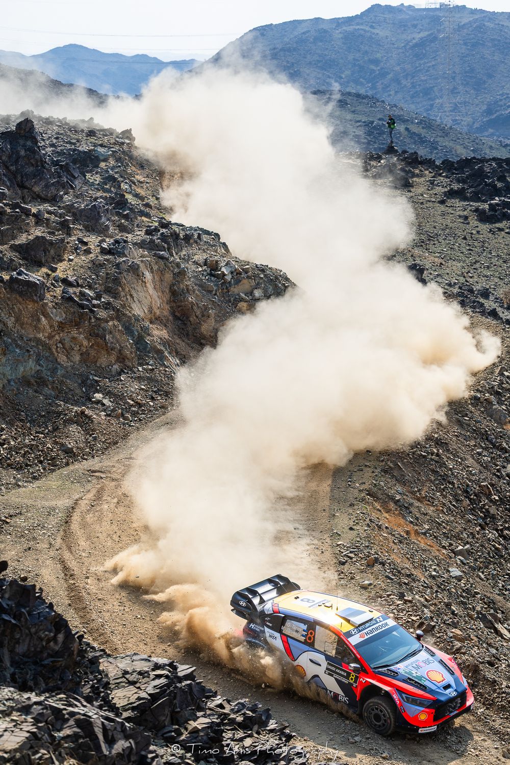 Rally car kicks up dust while navigating a steep mountain course during a challenging off-road competition.