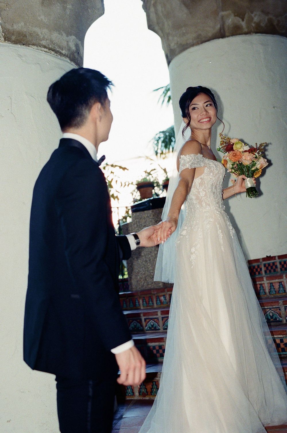 A 35mm film photo of a bride leading a groom up the staircase of the Santa Barbara Courthouse.