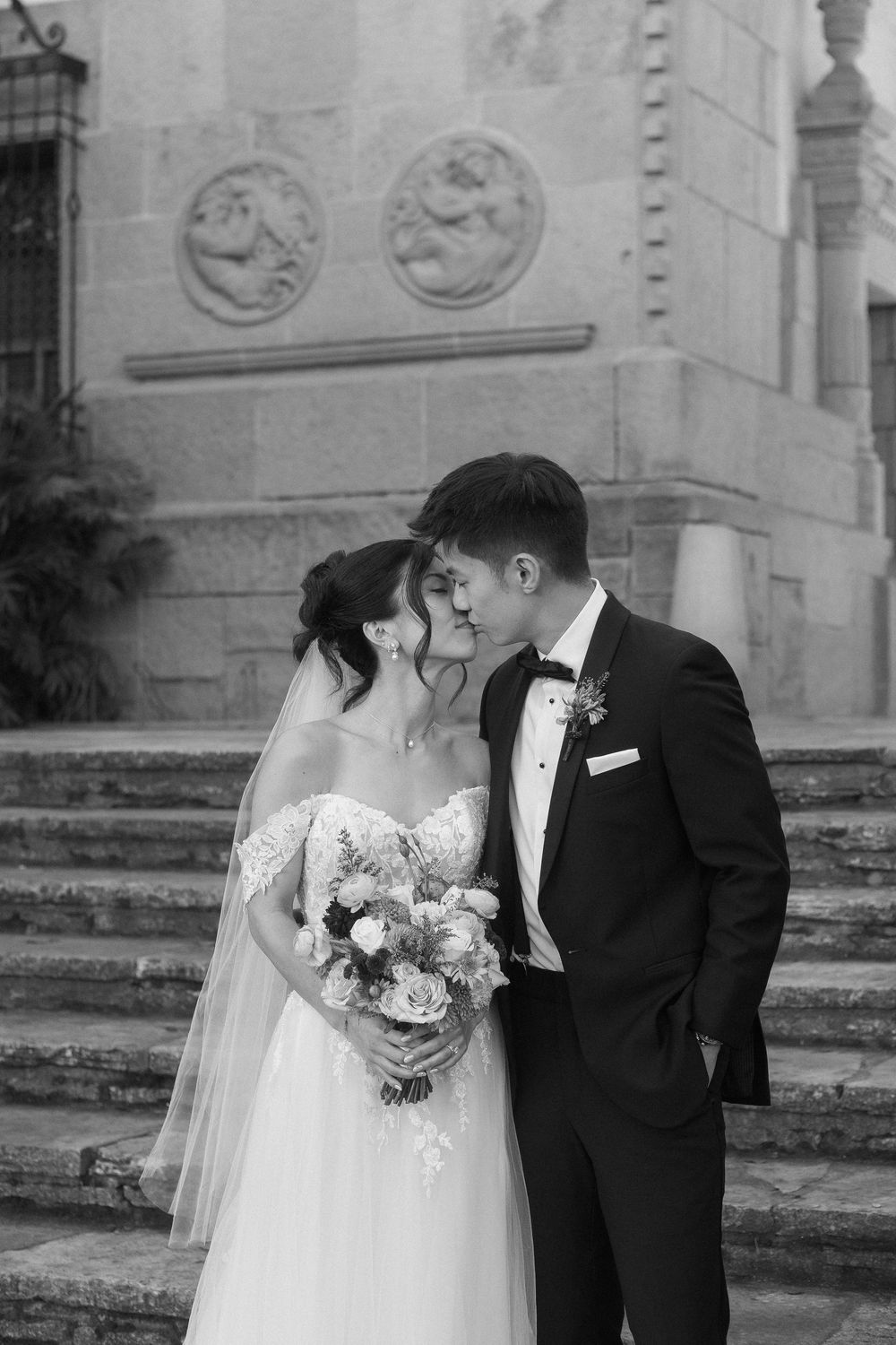 A black and white editorial photo of a bride and groom kissing at the Santa Barbara Courthouse stone steps
