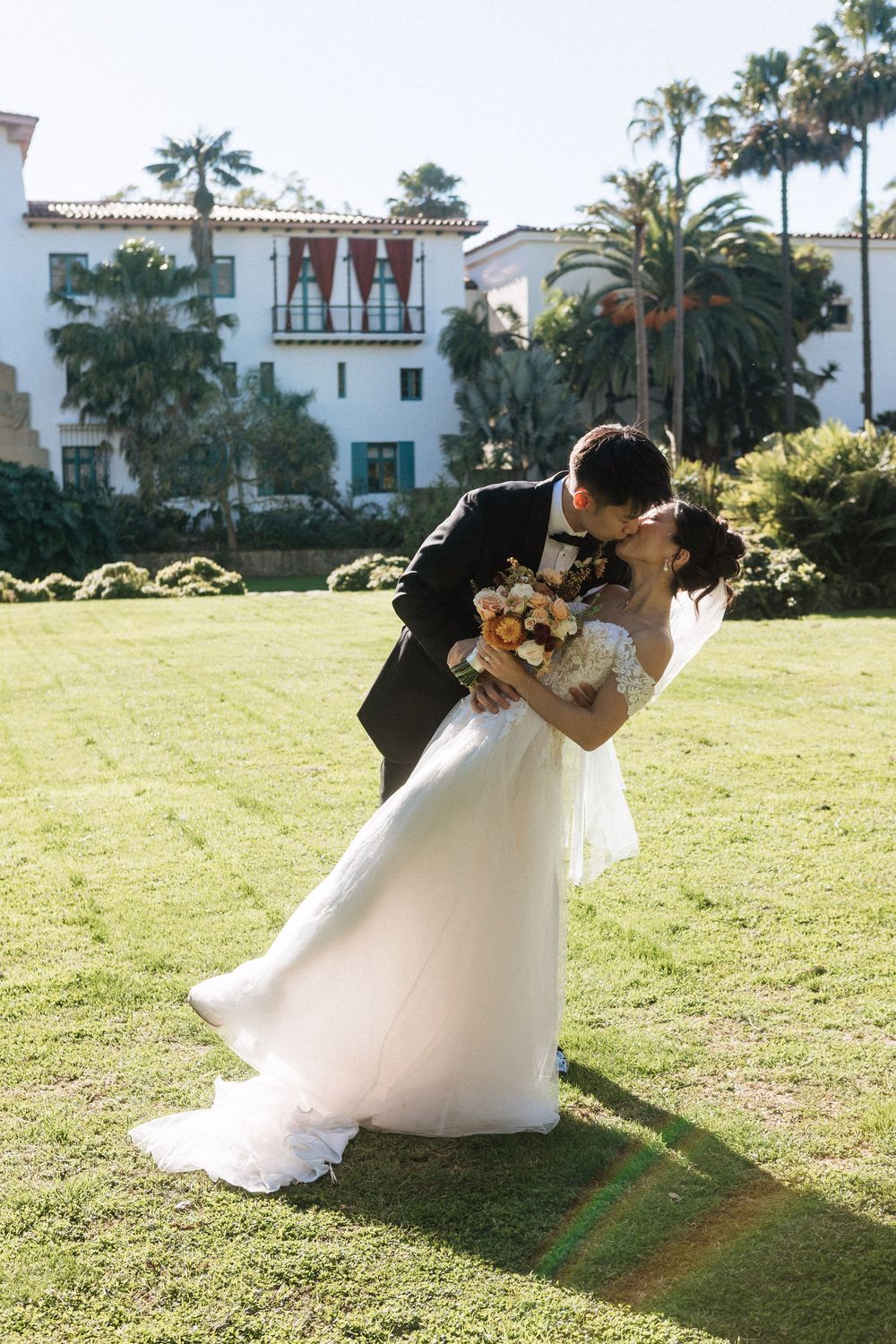 Bride in a lace gown and groom in a classic tux posing in the sunken gardens of the Santa Barbara Courthouse.