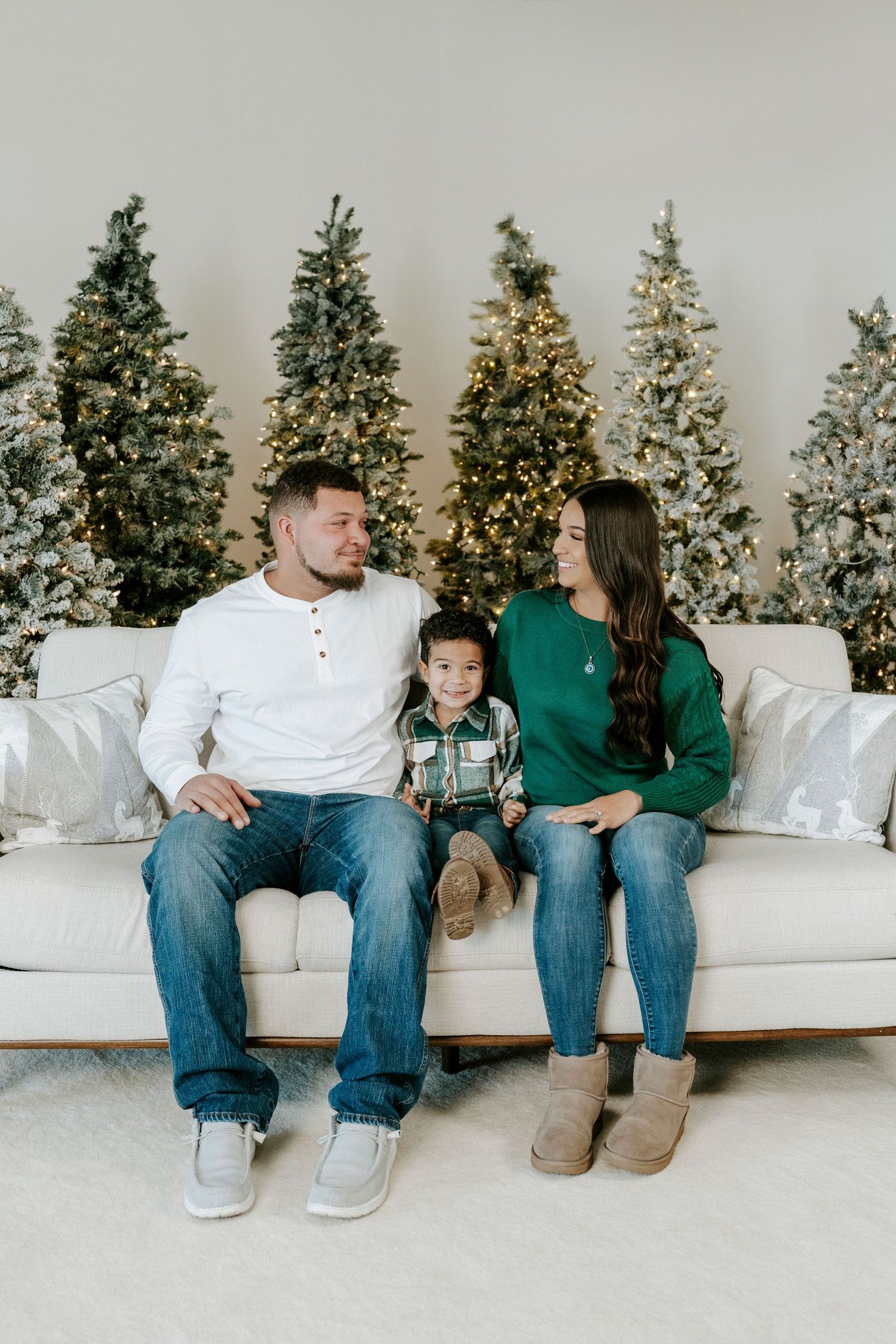 A cozy holiday scene with a family sitting on a white couch in front of five decorated Christmas trees.
