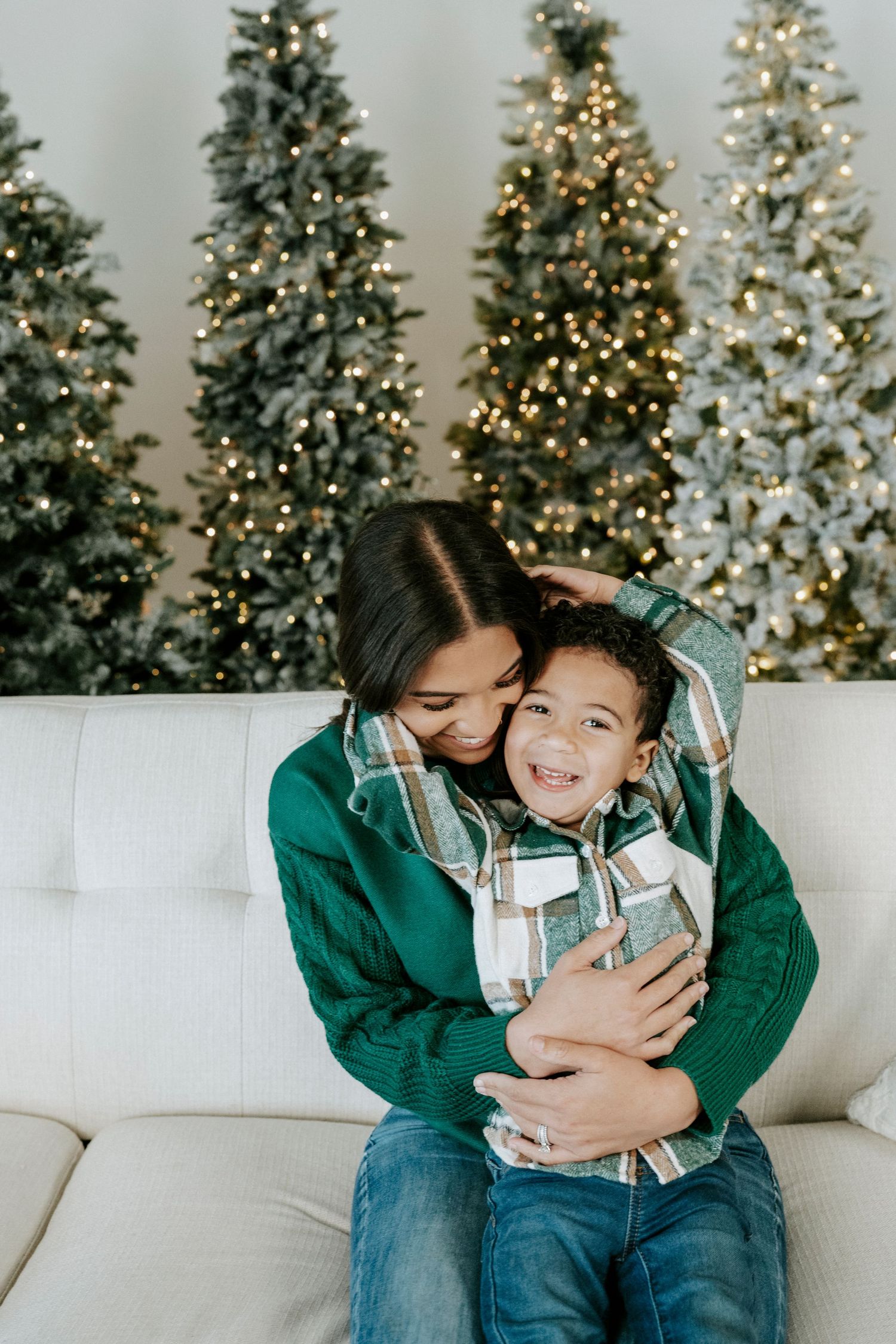 A warm embrace on a white couch with decorated Christmas trees glowing with lights in the background.