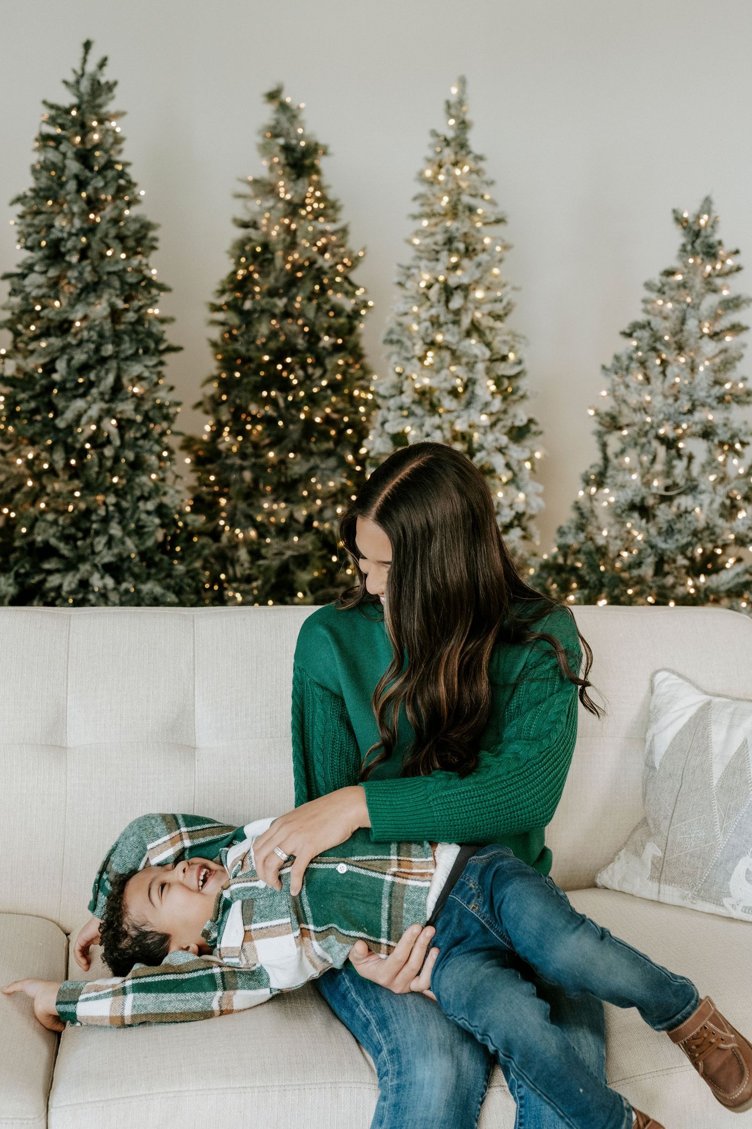 Family relaxing together on white couch with decorated Christmas trees in background.