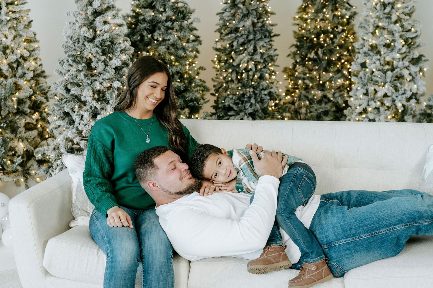 Couple relaxes together on white couch in front of decorated Christmas trees.