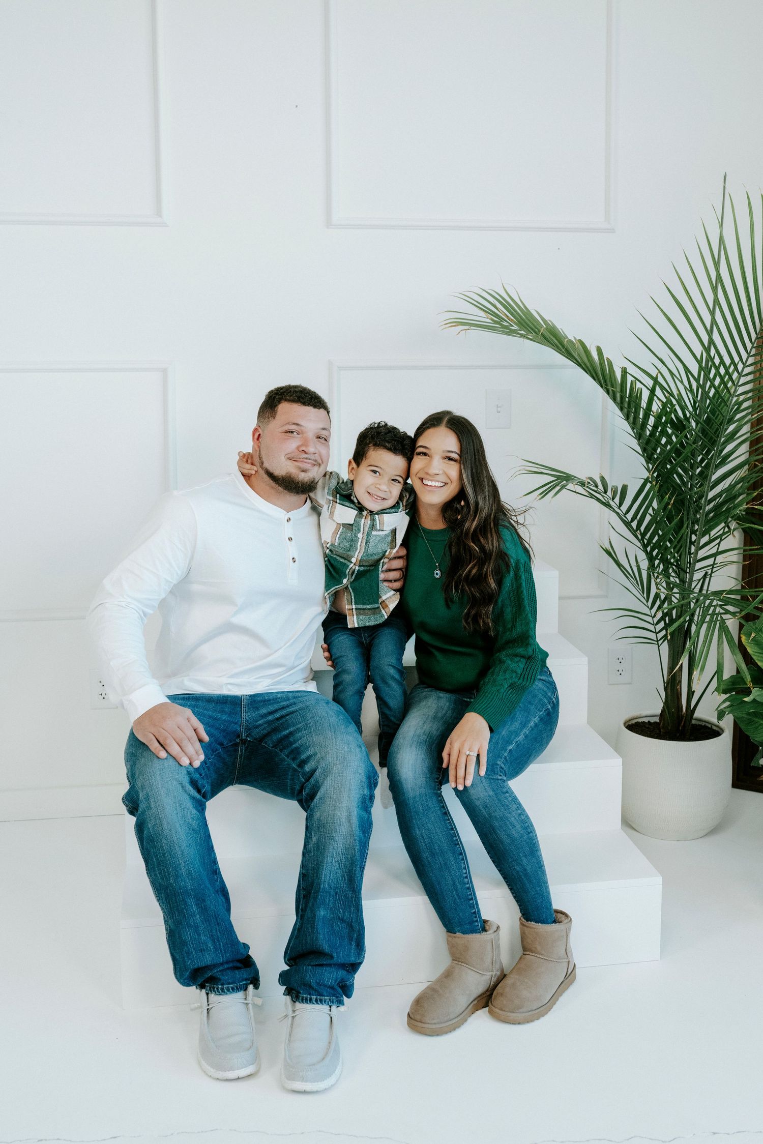 Family sitting together on white sofa in minimalist room with potted palm plant.