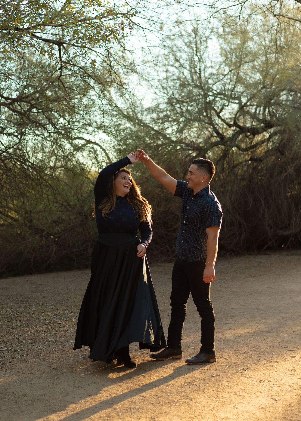 A couple dancing and twirling together on a desert path at sunset.