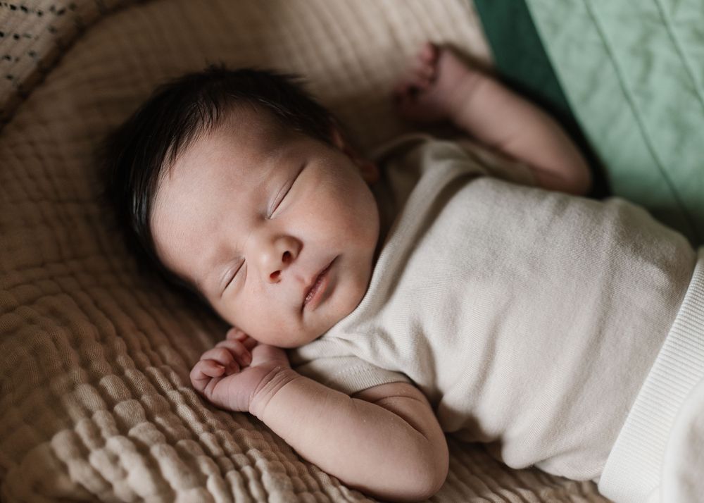 Peaceful newborn baby sleeping soundly, wrapped in a cream swaddle on a soft textured blanket.