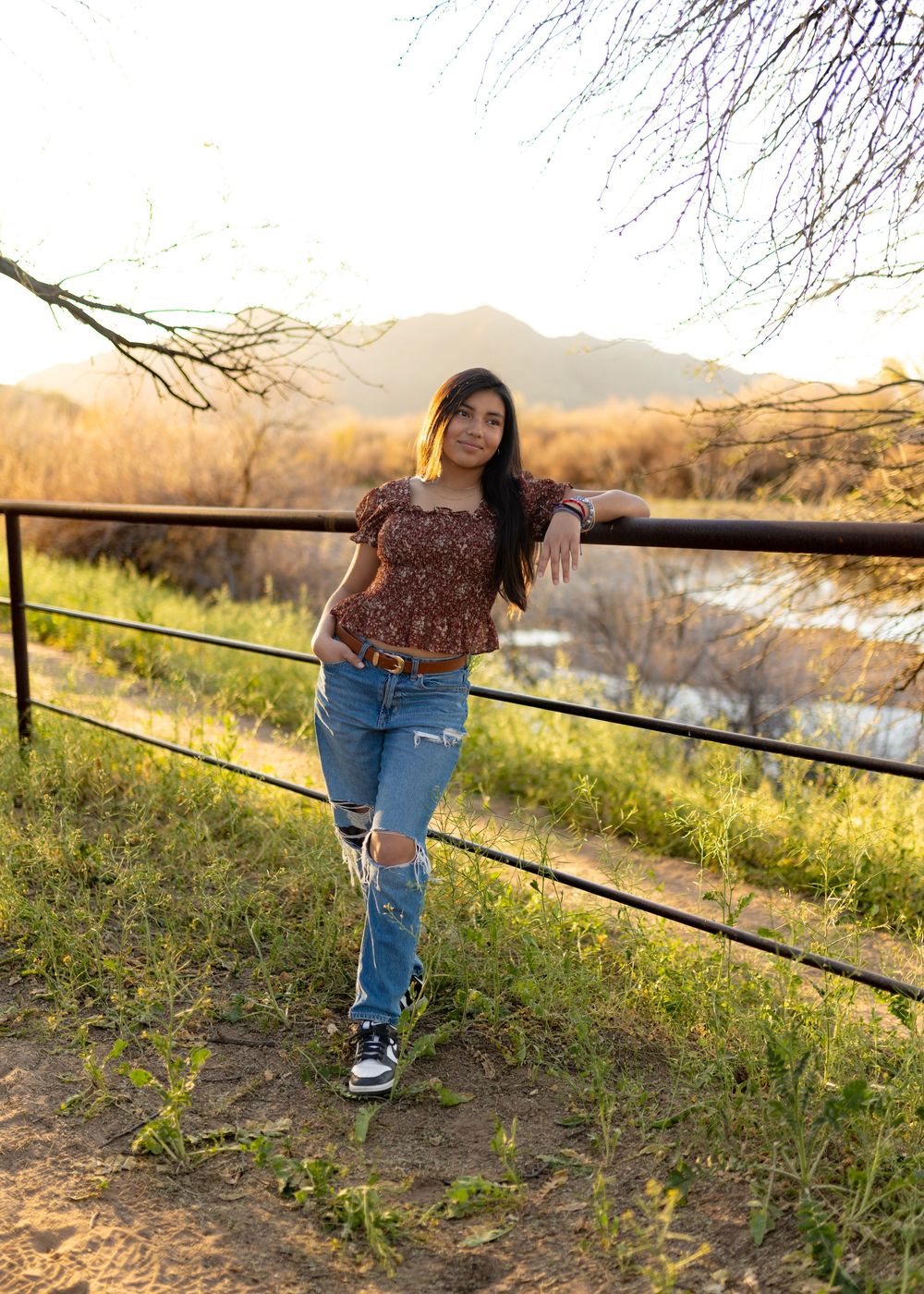 Person in casual attire leans against railing during sunset photoshoot.