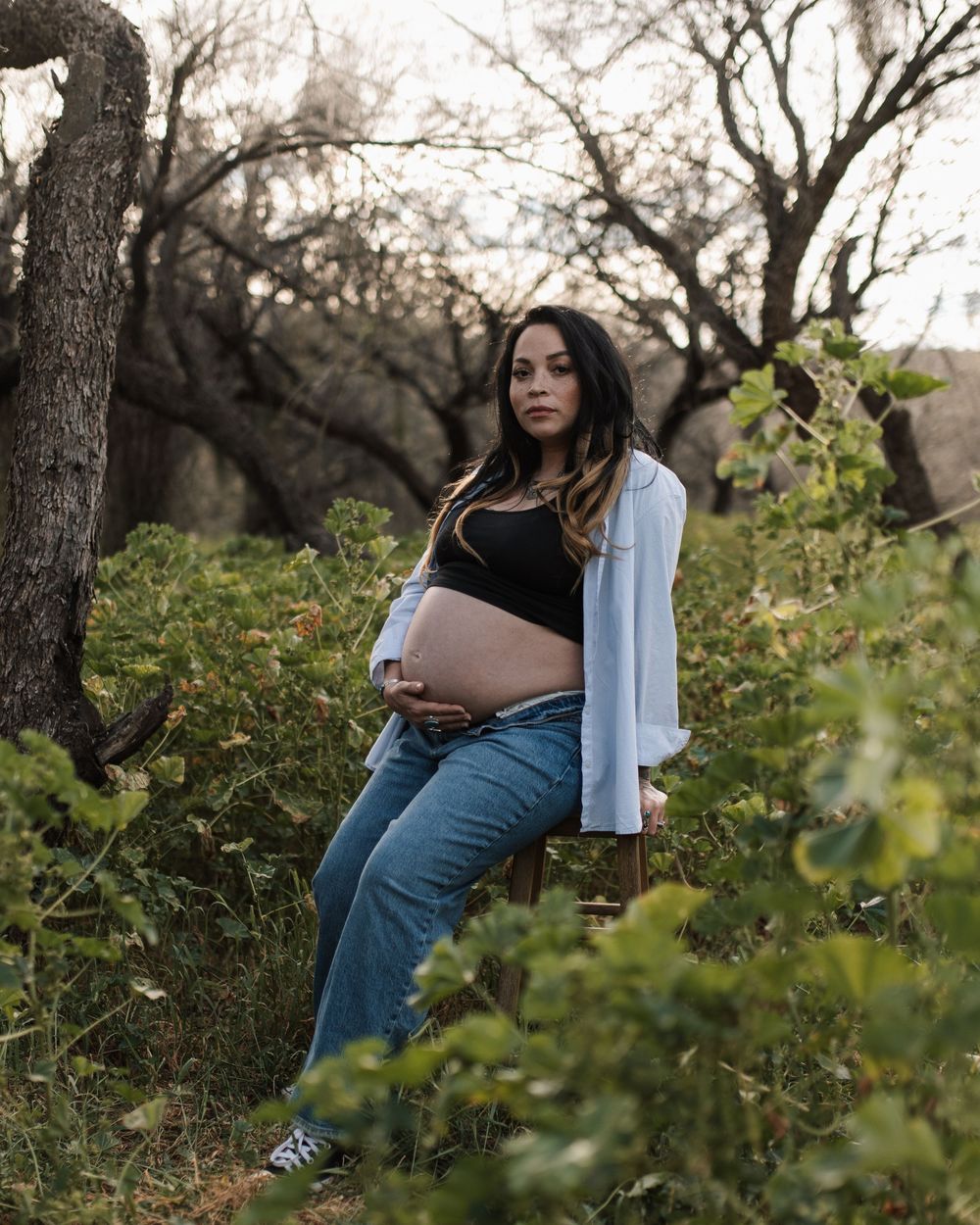 Maternity photo session in natural outdoor setting with trees.