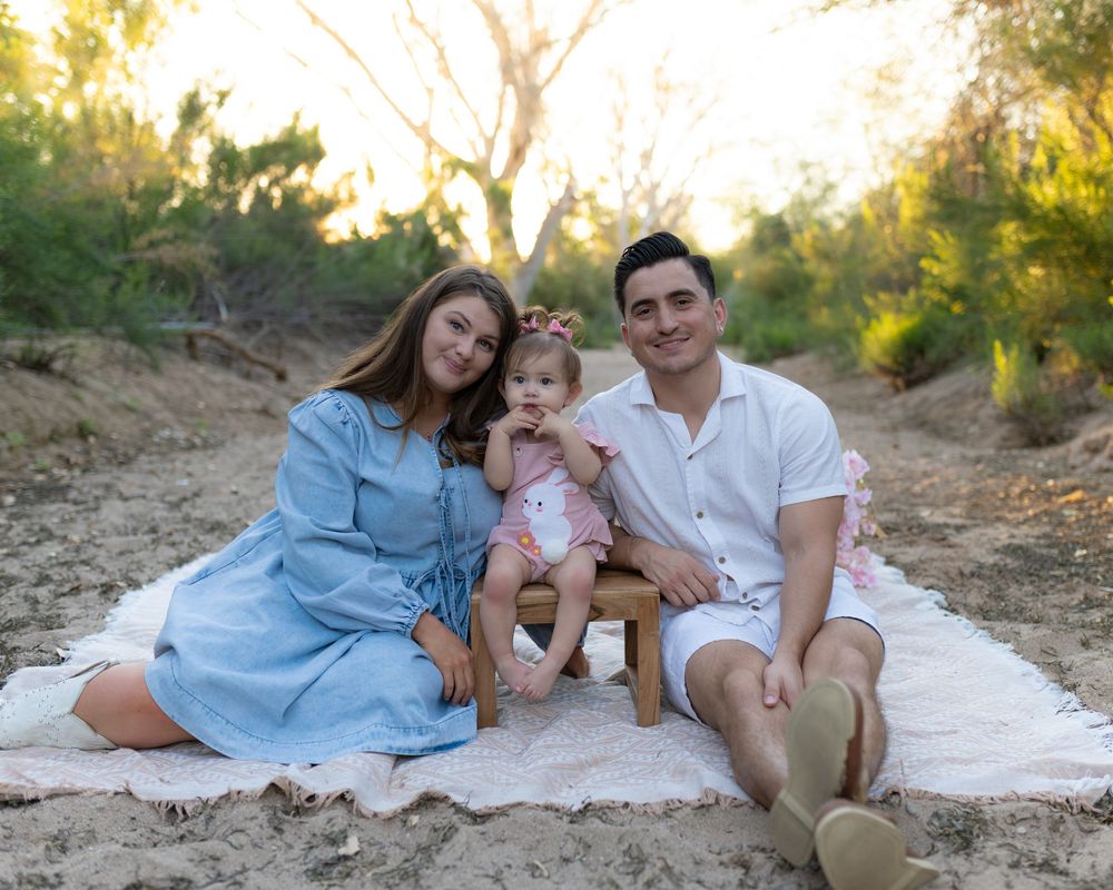 A family relaxes together on a white blanket during an outdoor photo session.